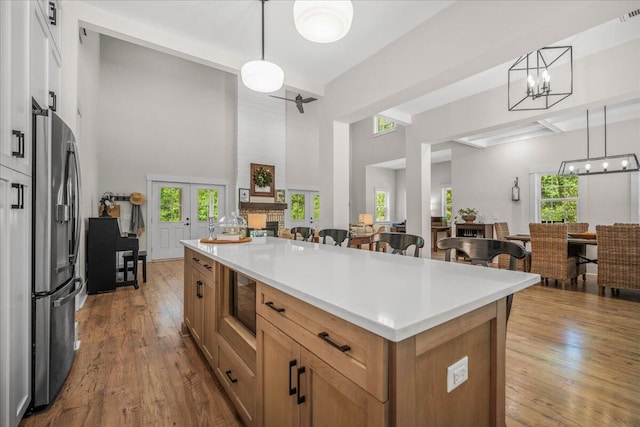 kitchen with stainless steel fridge with ice dispenser, a high ceiling, a chandelier, open floor plan, and wood-type flooring