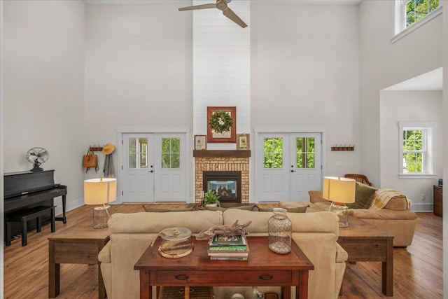 living area featuring a towering ceiling, wood finished floors, a ceiling fan, a brick fireplace, and baseboards