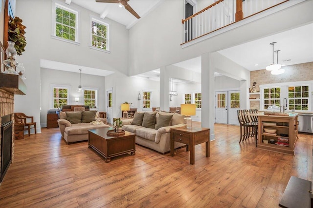 living area with a high ceiling, french doors, hardwood / wood-style floors, a ceiling fan, and a fireplace
