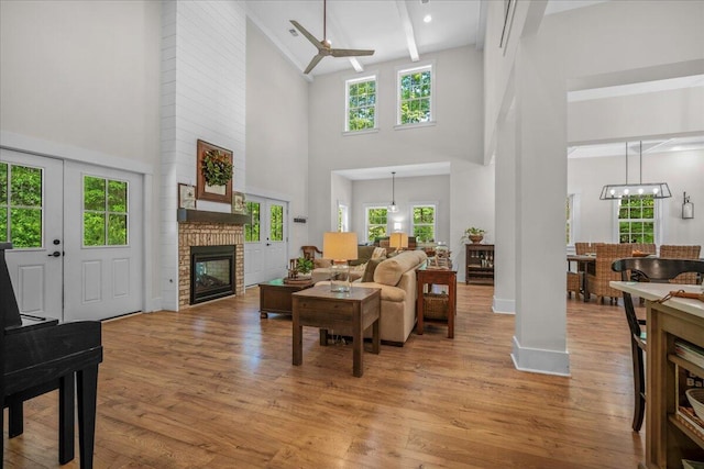 living room with a towering ceiling, a fireplace, light wood finished floors, plenty of natural light, and ceiling fan