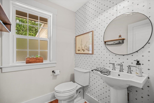 half bathroom with wallpapered walls, toilet, and baseboards