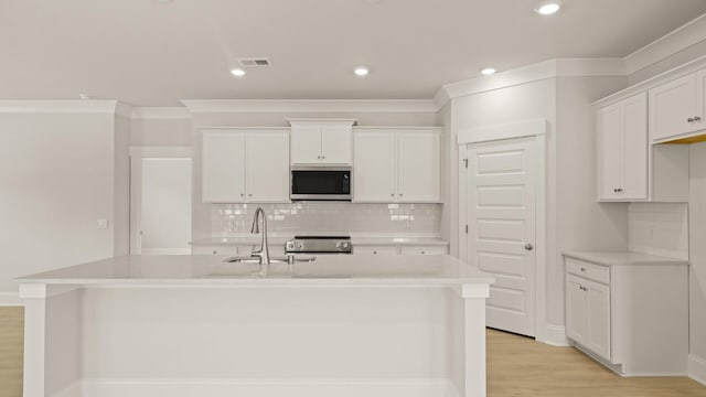 205 Bilge Rd, Ridgeville, SC 29472 - kitchen with stainless steel microwave, an island with sink, stove, tasteful backsplash, and white cabinetry