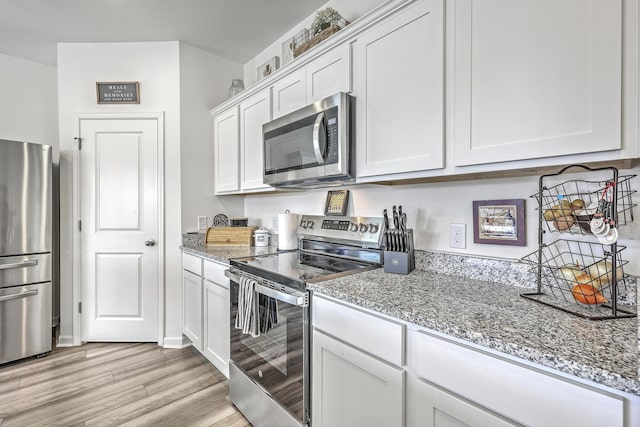 kitchen featuring light wood-style flooring, light stone countertops, white cabinets, and appliances with stainless steel finishes