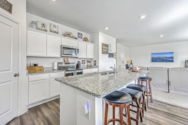 kitchen featuring a breakfast bar, wood finished floors, white cabinets, stainless steel appliances, and a sink