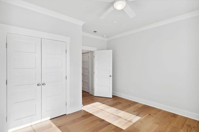 unfurnished bedroom with light wood-style flooring, a closet, baseboards, and crown molding