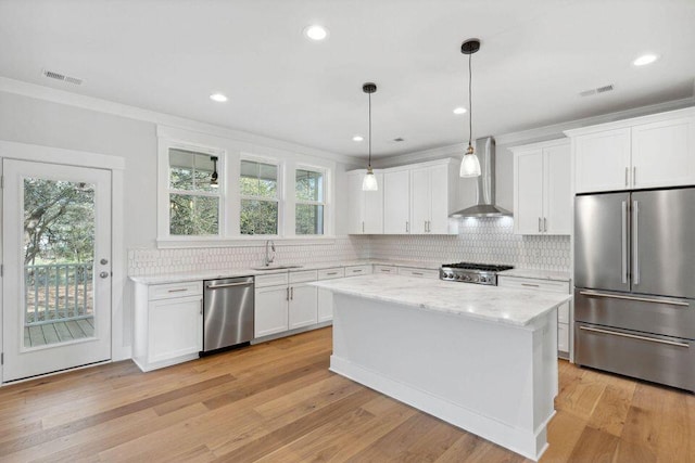 kitchen featuring appliances with stainless steel finishes, visible vents, a sink, and wall chimney range hood