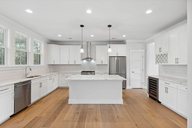 kitchen featuring wine cooler, stainless steel appliances, a sink, wall chimney range hood, and light wood finished floors