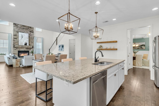 kitchen with a center island with sink, sink, light stone countertops, appliances with stainless steel finishes, and white cabinetry