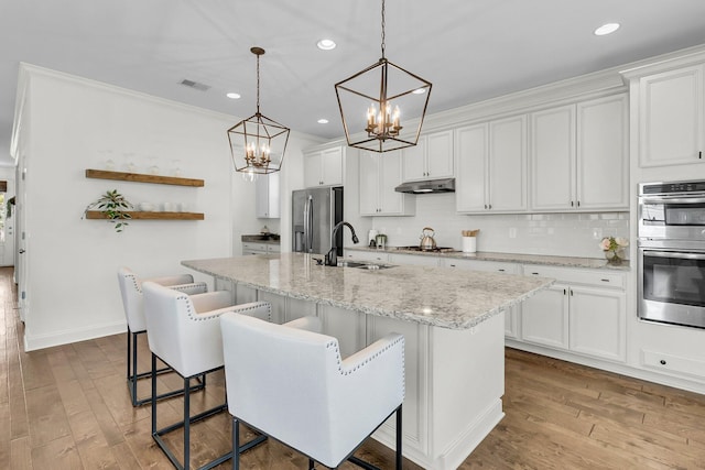 kitchen featuring white cabinetry, stainless steel appliances, an island with sink, and light hardwood / wood-style flooring