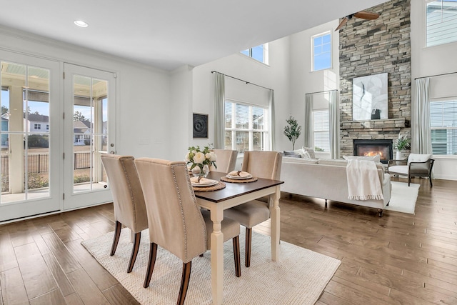 dining room featuring a stone fireplace, wood-type flooring, ornamental molding, and a wealth of natural light