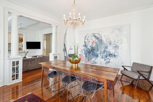 dining room with decorative columns, wood-type flooring, a notable chandelier, and ornamental molding