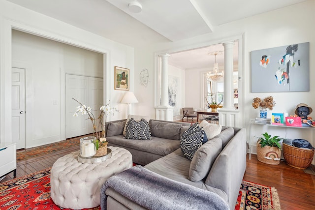 living room with a notable chandelier, dark wood-type flooring, and ornate columns