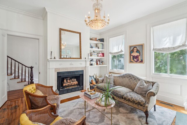 living room with a tile fireplace, an inviting chandelier, crown molding, and hardwood / wood-style flooring