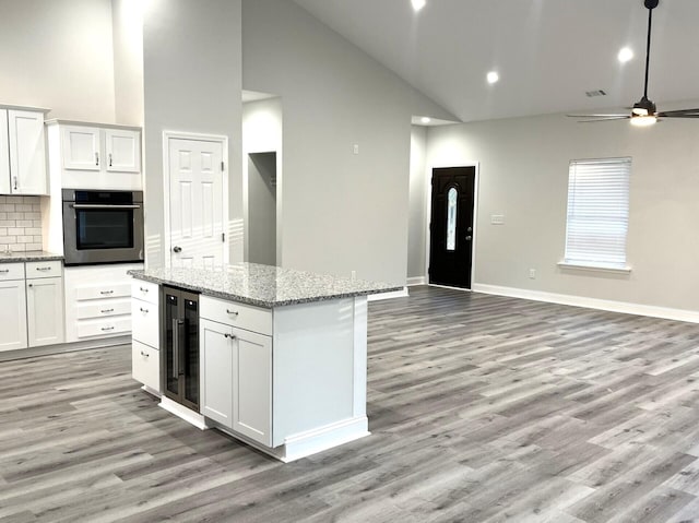 kitchen with wine cooler, light stone counters, a center island, oven, and white cabinets