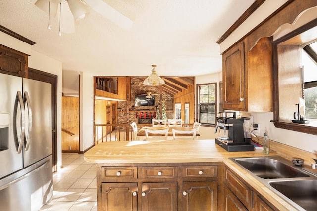 kitchen with wood counters, sink, stainless steel refrigerator with ice dispenser, light tile patterned floors, and brick wall