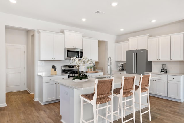 kitchen with stainless steel appliances, a sink, light wood-style floors, tasteful backsplash, and an island with sink