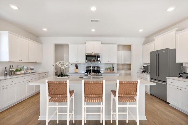 kitchen with stainless steel appliances, visible vents, light wood finished floors, and an island with sink