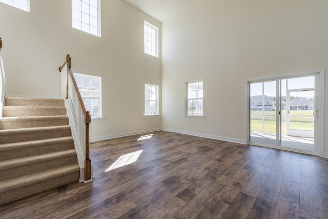 unfurnished living room featuring a towering ceiling, dark wood finished floors, stairway, and baseboards