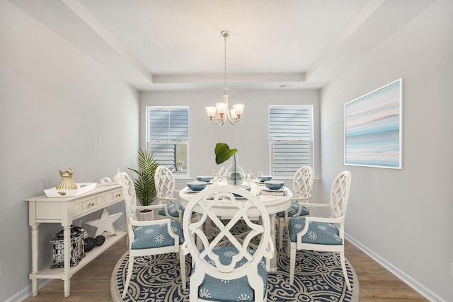 dining room featuring a tray ceiling, wood finished floors, baseboards, and an inviting chandelier