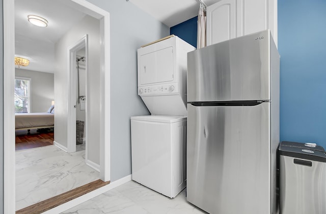 laundry area with stacked washer / dryer, marble finish floor, laundry area, and baseboards