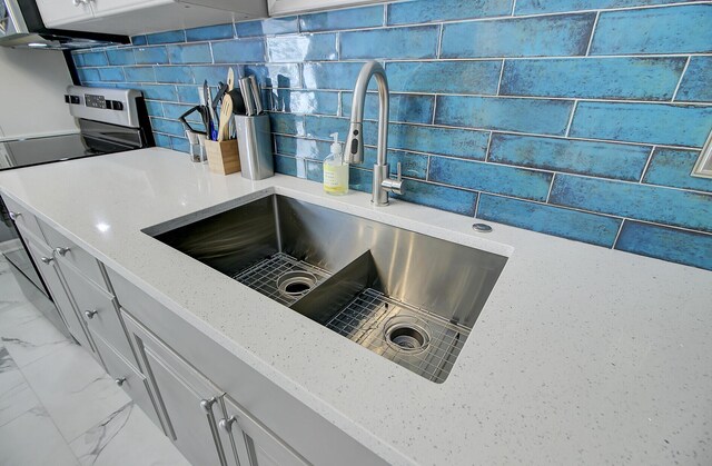 room details featuring tasteful backsplash, light stone countertops, electric range, white cabinetry, and a sink