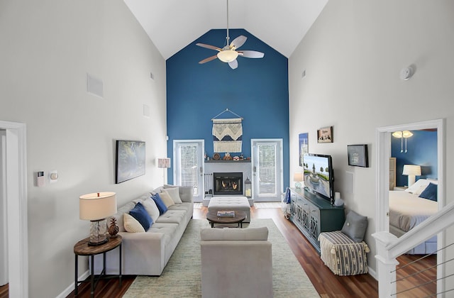 living area featuring a ceiling fan, wood finished floors, baseboards, and a warm lit fireplace