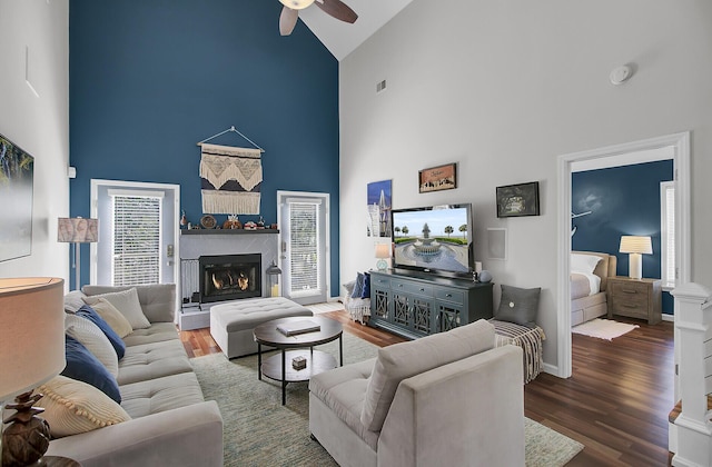 living room with baseboards, a lit fireplace, wood finished floors, high vaulted ceiling, and a ceiling fan