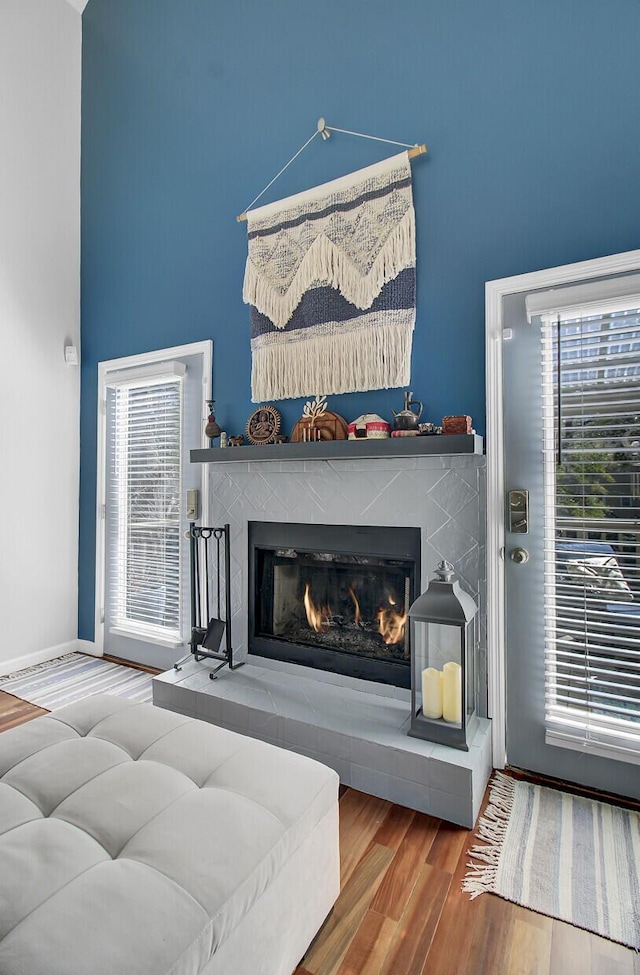 living area featuring a high ceiling, wood finished floors, baseboards, and a lit fireplace