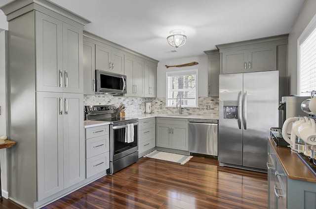 kitchen with a sink, appliances with stainless steel finishes, dark wood-style flooring, and gray cabinetry