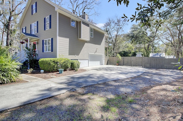 view of side of property featuring a chimney, concrete driveway, a garage, and fence