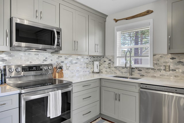 kitchen featuring gray cabinetry, light countertops, decorative backsplash, appliances with stainless steel finishes, and a sink