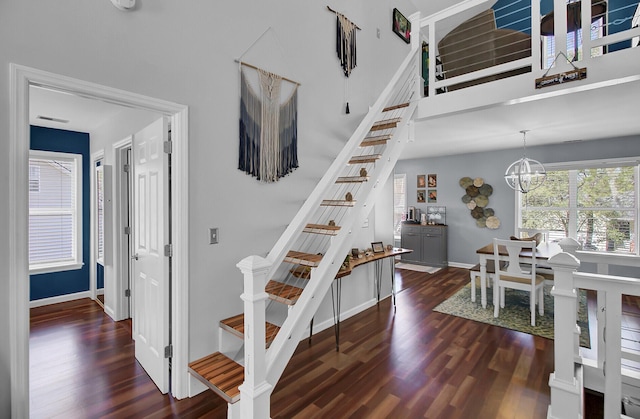 stairs with a notable chandelier, baseboards, a towering ceiling, and wood finished floors