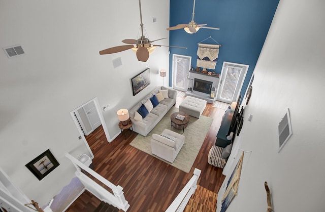 living area featuring visible vents, wood finished floors, a glass covered fireplace, and a towering ceiling