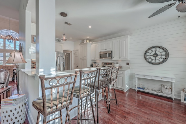 kitchen featuring appliances with stainless steel finishes, a breakfast bar, white cabinets, dark hardwood / wood-style flooring, and kitchen peninsula