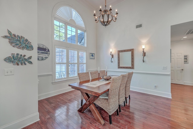 dining space featuring a high ceiling, hardwood / wood-style floors, and an inviting chandelier