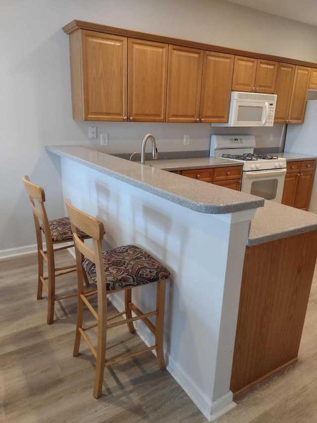 kitchen featuring light wood finished floors, baseboards, a kitchen bar, a peninsula, and white appliances