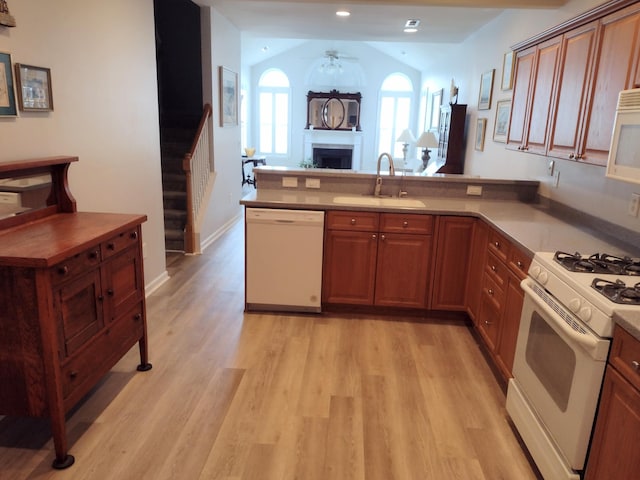 kitchen with light wood-style flooring, a fireplace, a peninsula, white appliances, and a sink