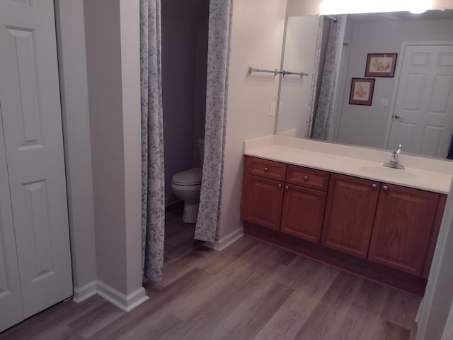 bathroom with toilet, vanity, baseboards, and wood finished floors