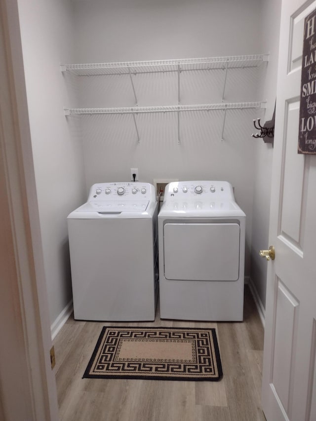 washroom featuring washer and dryer, laundry area, wood finished floors, and baseboards