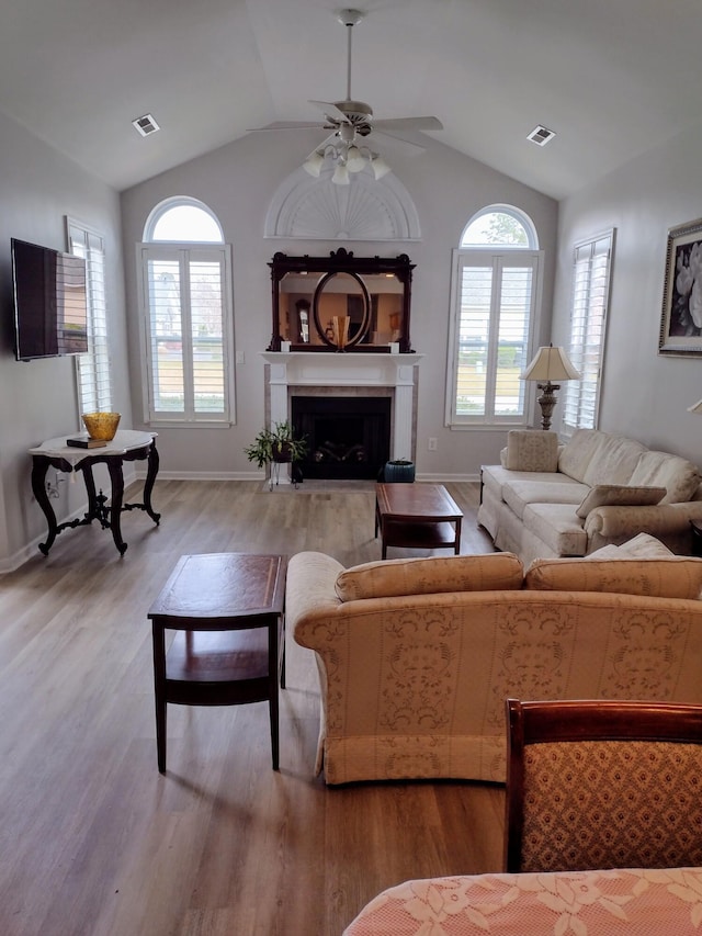 living area with visible vents, lofted ceiling, a fireplace with flush hearth, and wood finished floors