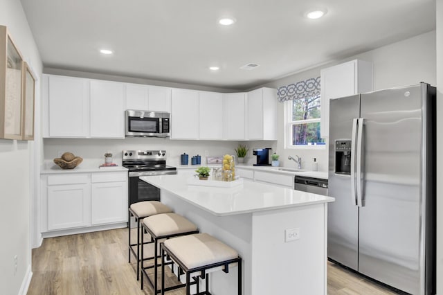 kitchen featuring a center island, white cabinetry, a kitchen breakfast bar, light wood-type flooring, and appliances with stainless steel finishes