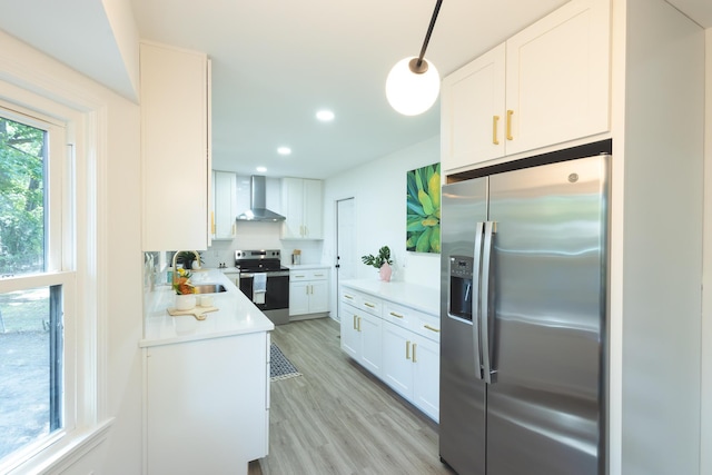 kitchen featuring stainless steel appliances, wall chimney range hood, a sink, light wood-style floors, and white cabinets