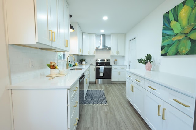 kitchen featuring stainless steel appliances, a sink, wall chimney exhaust hood, light wood-type flooring, and white cabinetry