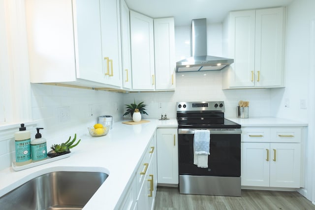 kitchen with electric range, wall chimney exhaust hood, light wood finished floors, and light countertops