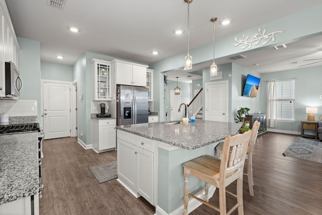 kitchen with light stone countertops, white cabinets, stainless steel appliances, an island with sink, and backsplash