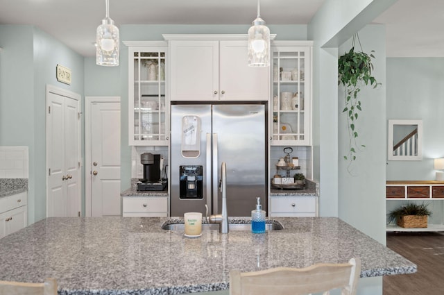 kitchen with white cabinets, backsplash, stainless steel fridge, and light stone countertops