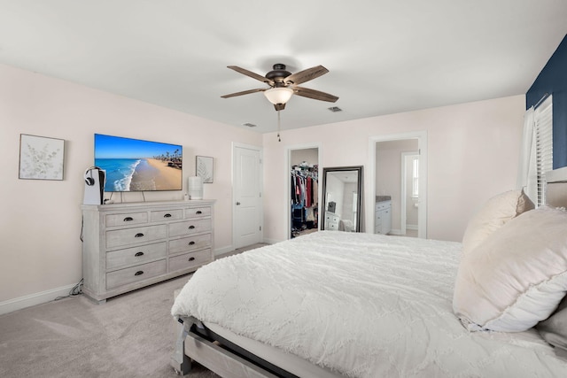 bedroom with a spacious closet, ensuite bath, light carpet, a closet, and ceiling fan