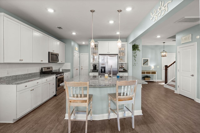 kitchen featuring white cabinetry, an island with sink, stainless steel appliances, decorative backsplash, and pendant lighting