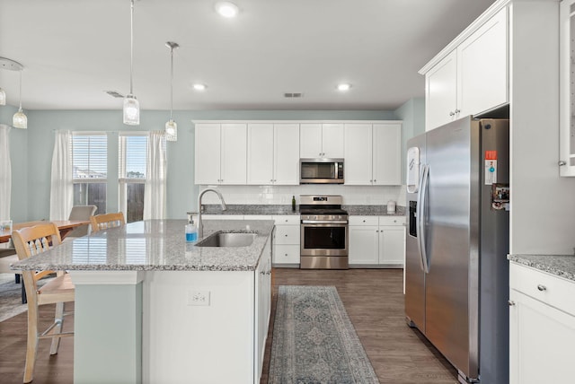 kitchen with sink, hanging light fixtures, appliances with stainless steel finishes, and a kitchen island with sink