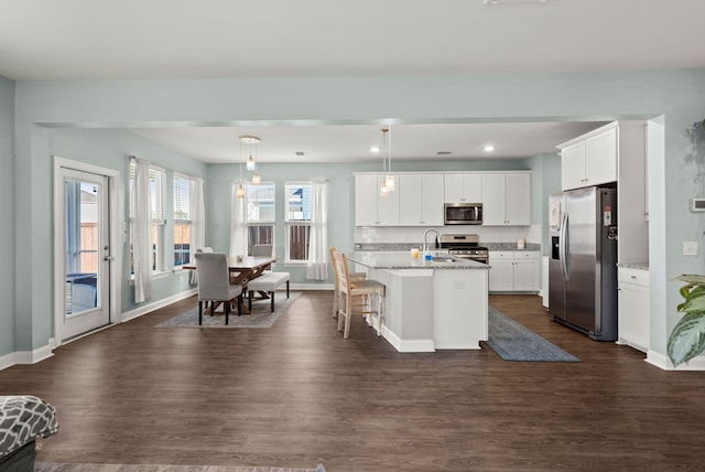 kitchen featuring hanging light fixtures, dark wood-type flooring, an island with sink, a breakfast bar area, and stainless steel appliances